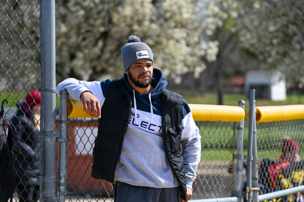 Coach Aaron Eden leaning on a fence at a youth baseball practice – AE Training, Warrensburg, MO